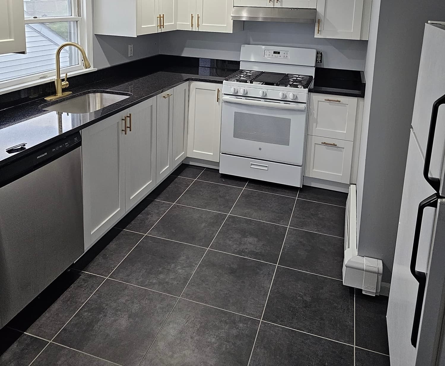 Kitchen remodel with white cabinets, black countertops and dark tile floor